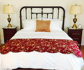 Bed made with a red comforter and a night stand on both sides.